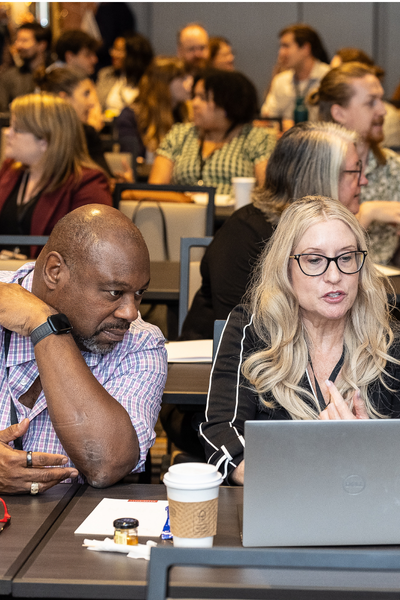 Middle age black man looking at a computer with a white, middle age woman talking.